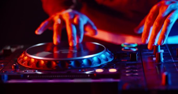 Disc jockey working on his professional mixer controller, sliding the panels and turning knobs in nightclub red and blue lights - nightlife concept 4k footage close up shot