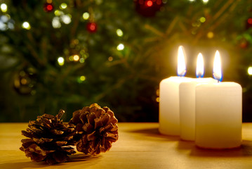 three burning candles with Christmas decoration from pine cones around