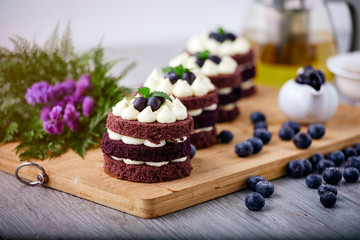 Row of four brown cakes with blue berry on top placing together pink flower and berry as decorated item on the wooden plate.