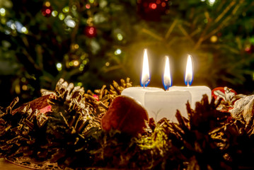 three burning candles with Christmas decoration from pine cones around