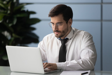 Serious male employee busy using modern laptop in office