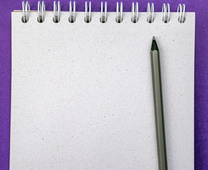 top view of black pencil on grey notebook on purple background.