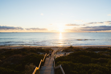 Young woman walking down the beach staircase and path to the sea with the orange sunset over the beautiful ocean in Perth, Western Australia.  