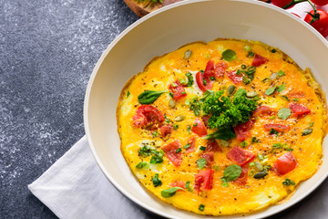 omelet with tomatoes, greens, spinach and pumpkin seeds in frying pan on black background
