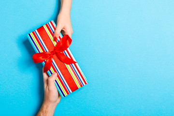 Top view of holding a gift in female and male hands on colorful background. Woman and man give and...