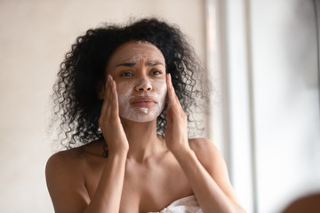 African American woman apply facial cream in bathroom