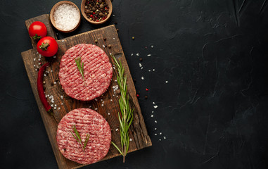 Raw beef burger cutlets with herbs and spices on a concrete background