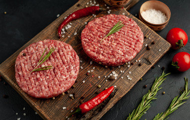 Raw beef burger cutlets with herbs and spices on a concrete background