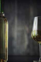 Transparent bottle of white dry wine on the table. White wine glass on a wooden background.