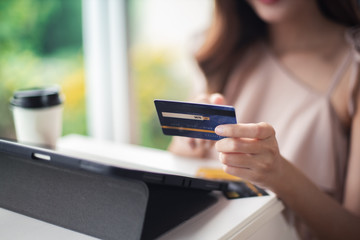 Happy Asian young woman doing online shopping at home.She holding credit card and using laptop computer.Smiling asian woman on couch using tablet to shop online n the living room.