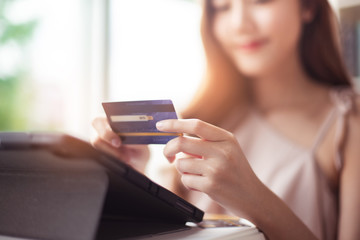 Happy Asian young woman doing online shopping at home.She holding credit card and using laptop computer.Smiling asian woman on couch using tablet to shop online n the living room.