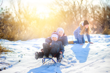 Children play in a snowy winter park at sunset. Sledding down the hill and having fun. Winter fun. Holidays.