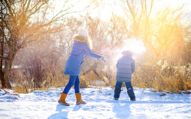 Fototapeta na wymiar Children play in a snowy winter park at sunset. Throw snow and have fun. Winter fun. Holidays.