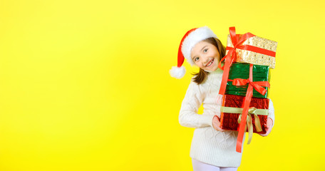 Cute little girl in a santa claus checker holds gift boxes in multi-colored wrapping papers and smiles cheerfully. Yellow studio background. Gifts concept.
