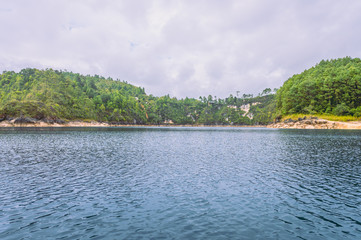 Beautiful landscape of a blue lake, in the background wooded mountains in cloudy sky day