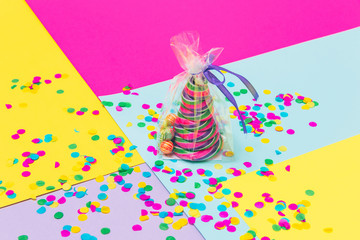 Candy Christmas treat in the shape of pine tree with little lollipops and confetti in plastic bag on geometric background. Minimalist. Happy holidays
