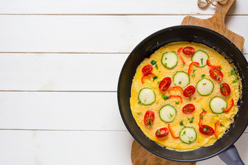 Omelette with zucchini, lamb's lettuce, tomatoes and red pepper in a pan. Frittata - italian omelet. Flat lay