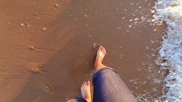 Slow motion. The girl is walks near sea and waves roll on her feet