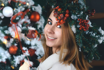 Smiling beautiful girl with mistletoe crown in front of Christmas tree