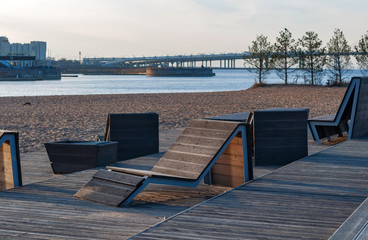Fototapeta na wymiar City beach on a frosty day at sunset, empty wooden sun loungers in soft sunlight
