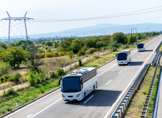 Three white buses in line on a country highway under a beautiful sky
