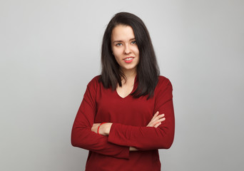 Obraz premium Young beautiful dark-haired girl stands straight with arms crossed wearing a red cotton stitch deep v-neck sweater on a gray background