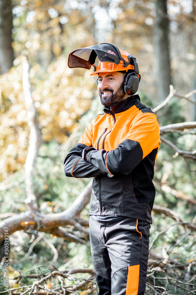 Poster portrait of a professional lumberman in harhat and protective workwear standing in the pine forest