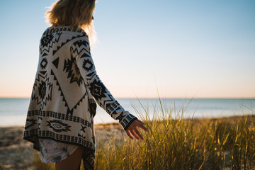 Young woman with blonde hair on an evening walk at sunset on the beach exploring the sand dunes and...
