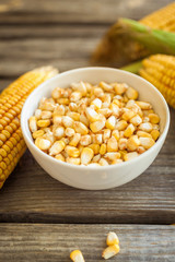 Raw corn on the cob and grains of corn in white bowl on wooden table