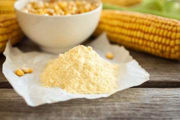 Corn flour and corn on the cobs on wooden background