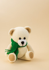 Crocheted toy bear in a green scarf on a light background