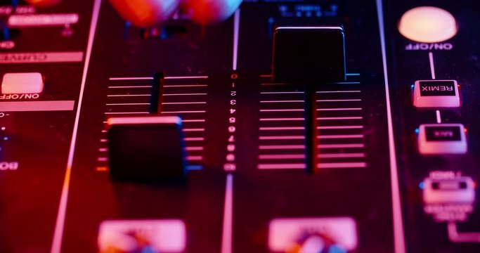Disc jockey working on his professional mixer controller, sliding the panels and turning knobs in nightclub red and blue lights - nightlife concept 4k footage close up shot