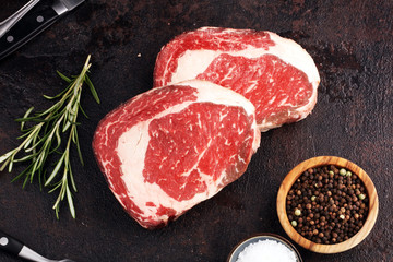 Raw fresh meat Ribeye Steak, seasoning and meat fork on rustic background