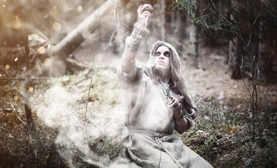Fototapeta na wymiar Fairy magician. A sorcerer with a glass sphere, a magical spell and a ritual. Elder with a staff and a cross in the forest. Black and white magic. A spell in an old book.