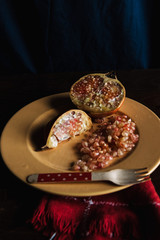 Rustic still life with a split pomegranate and a mustard-colored plate on a wooden table and a dark blue background.