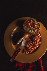 Rustic still life with a split pomegranate and a mustard-colored plate on a wooden table and a dark blue background.