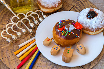 Festive donut, menorah, candles, jar of olive oil, dreidels - traditional symbols of Hanukkah Holiday. Hebrew letters on four sides of dreidel in English mean - Great Miracle Happened Here