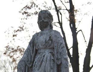 Monument and candles in the cemetery. All Saints Day in Poland. Stone statue in the cemetery. Stone statue in the cemetery. Close-up. Disfigured face statue.