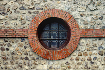circle porthole window with bars and ornaments on wall and stone and bricks around
