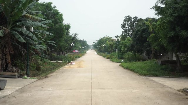 Wideshot of an Empty, Quiet Vietnamese Village Road Surrounded by Trees and with People in Background