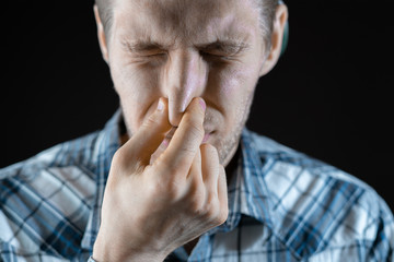 man close his nose on dark background, stink smell, fells disgusting sweat