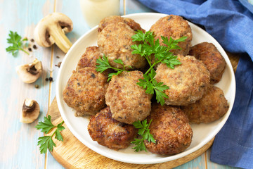 Homemade meatballs with mushrooms on the kitchen wooden table.
