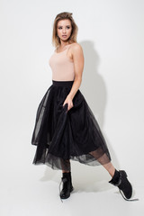 Beautiful girl in a light t-shirt and black skirt posing on a white background. Fashion shooting