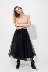 Fototapeta premium Beautiful girl in a light t-shirt and black skirt posing on a white background. Fashion shooting