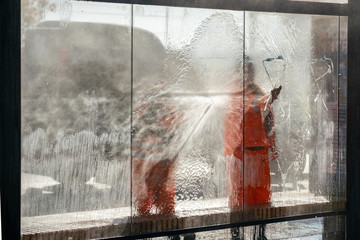 the city cleaning service man in orange uniform washing the bus stop glass with pouring water