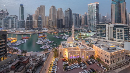 Yachts in Dubai Marina flanked by the Al Rahim Mosque and residential towers and skyscrapers aerial day to night timelapse.
