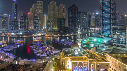 Fototapeta na wymiar Yachts in Dubai Marina flanked by the Al Rahim Mosque and residential towers and skyscrapers aerial night timelapse.