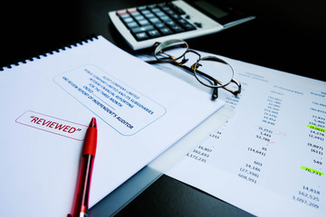 Red pencil placed on reviewed financial statement with eyeglasses, calculator and the edited paper. It's important work of the account, finance, internal and external audit must to accurate and timely