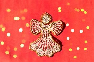 Christmas angel knitted bauble on red New Year background with bright lights, flat lay, top view