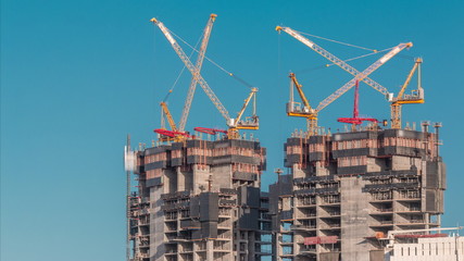 Aerial view of a skyscraper under construction with huge cranes timelapse in Dubai marina.